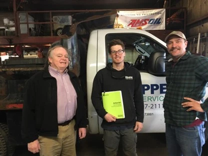 Three men, including one holding a bright yellow notebook labeled 'Arborist', standing in front of a Hoppe Tree Service truck