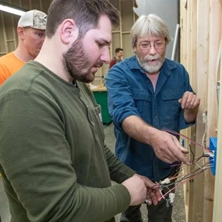 Three men installing wires in an electrical box